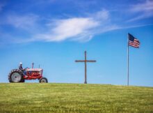 Ford tractor on hill with cross and flag